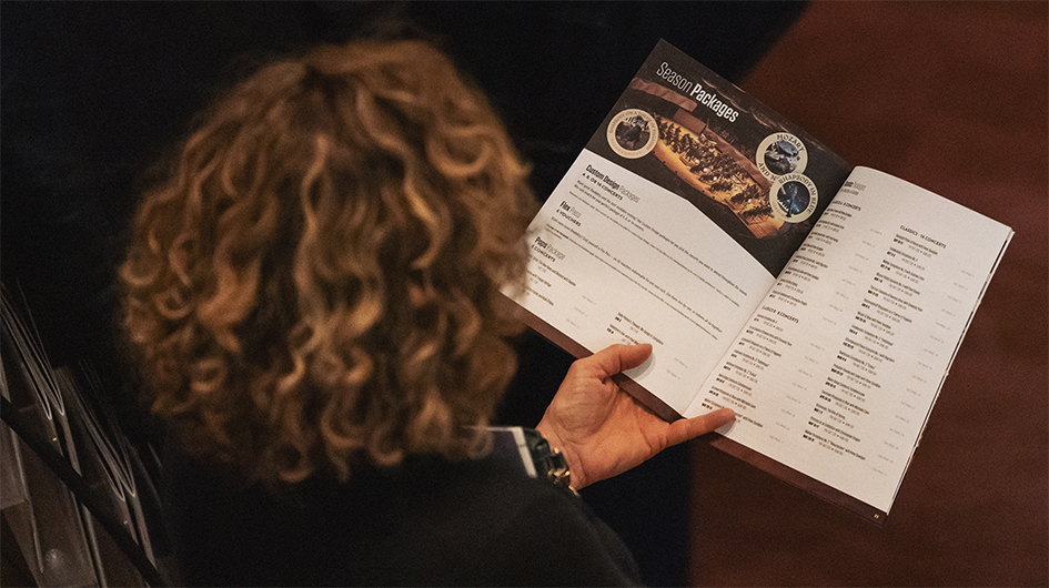 Patron holding a Colorado Symphony season brochure with the spread open to the Subscription Packages page.