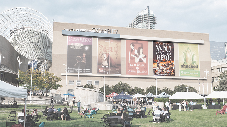 A photo of the Denver Perfoming Arts Complex taken from Sculpture Park and focusing on the west wall of Boettcher Concert Hall which displays five large banners. The entire image is faded except for one banner on the wall. The banner is a closeup image of the orchestra on stage with large text above which reads 
