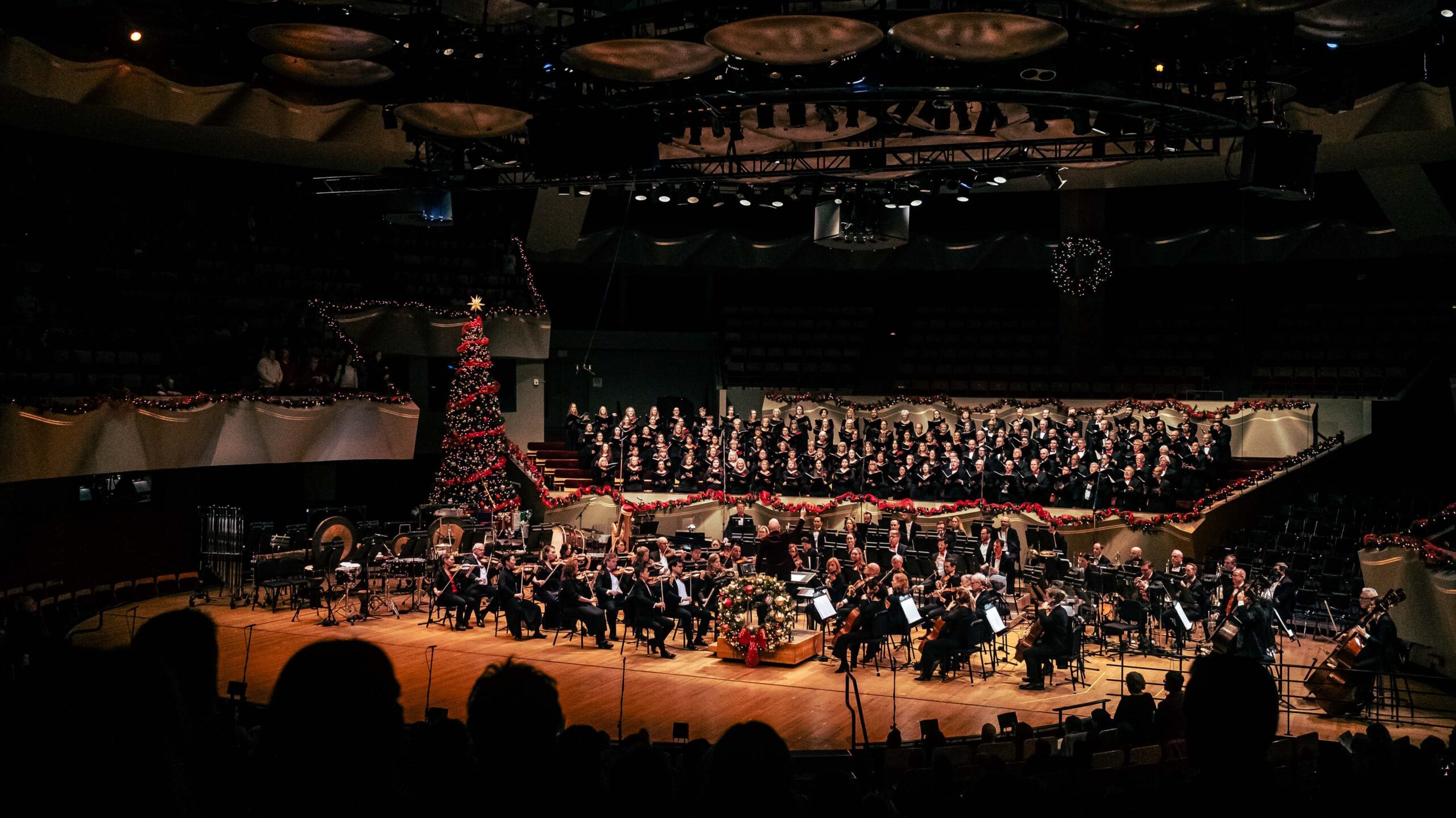 The Colorado Symphony performs with the Colorado Symphony Chorus and the Colorado Children's Chorale in Boettcher Concert Hall during Christmas, featuring festive decorations including a large Christmas tree.