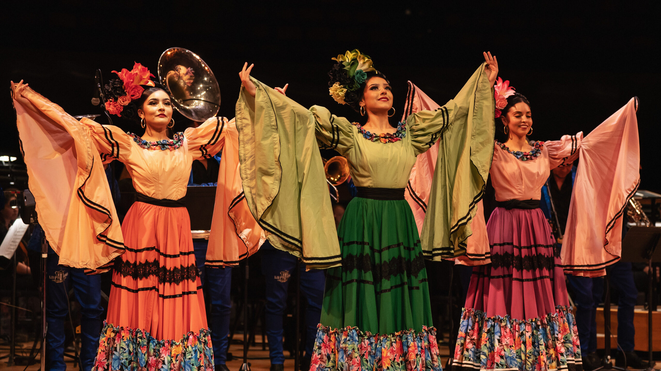 Dancers wearing traditional Latin American dresses perform on stage at Boettcher Concert Hall