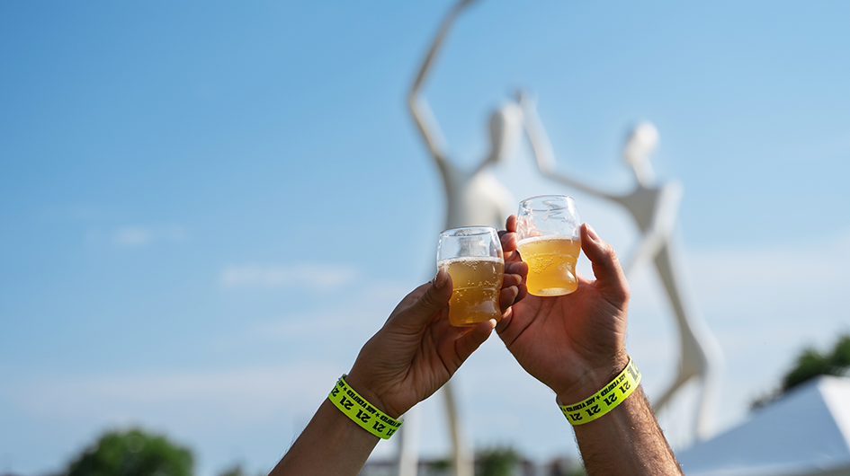 Two people toasting two sample size glasses of beer in Denver's Sculpture Park