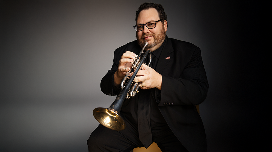 Principal Trumpet Justin Bartels poses with his trumpet while wearing concert black.