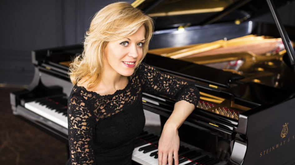 Pianist Olga Kern poses at the piano wearing a black lace top.