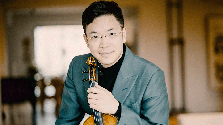 Violinist Paul Huang poses with his violin while wearing a black shirt and soft green blazer.