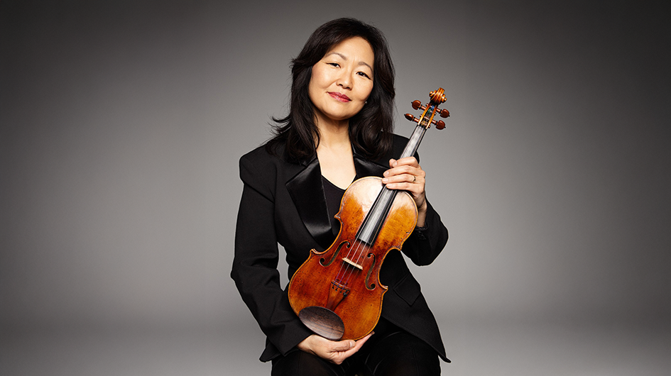 Concertmaster Yumi Hwang-Williams poses with her violin in front of a gray background.