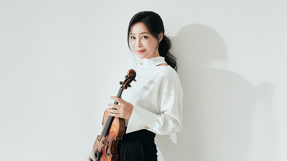 Violinist Soyoung Yoon poses with her violin while wearing a white shirt in front of a light gray background.