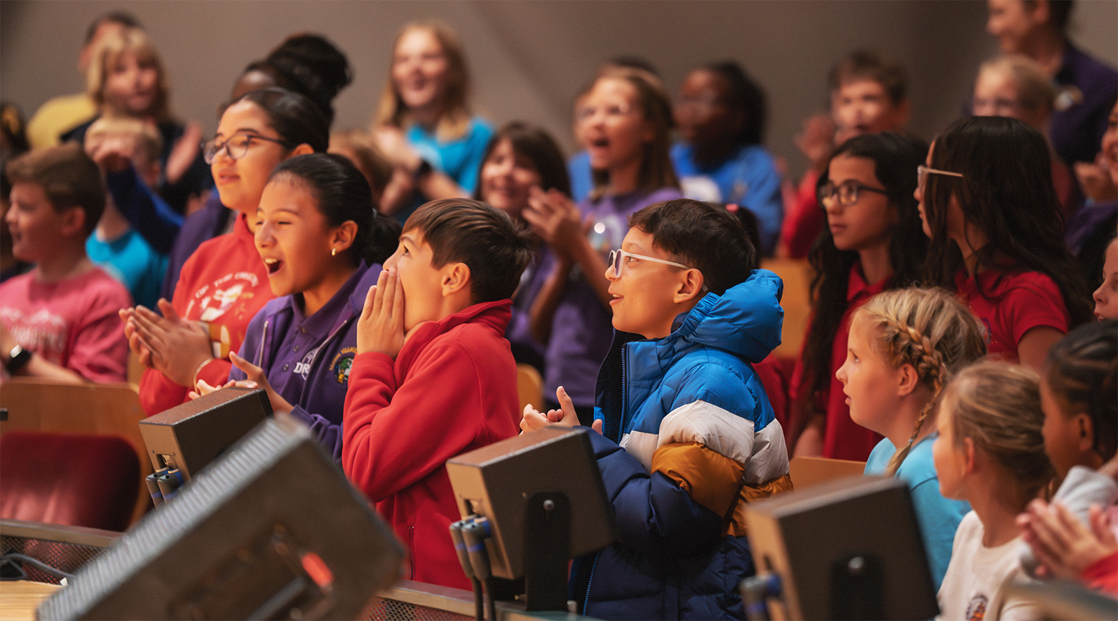 Students in the front few rows of Boettcher Concert Hall are standing, laughing, and clapping during a Youth Concert.