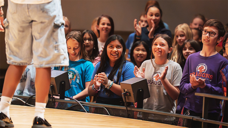 Closeup image of students stand, clapping, and smiling in the front few rows of Boettcher Concert Hall during a Youth Concert.